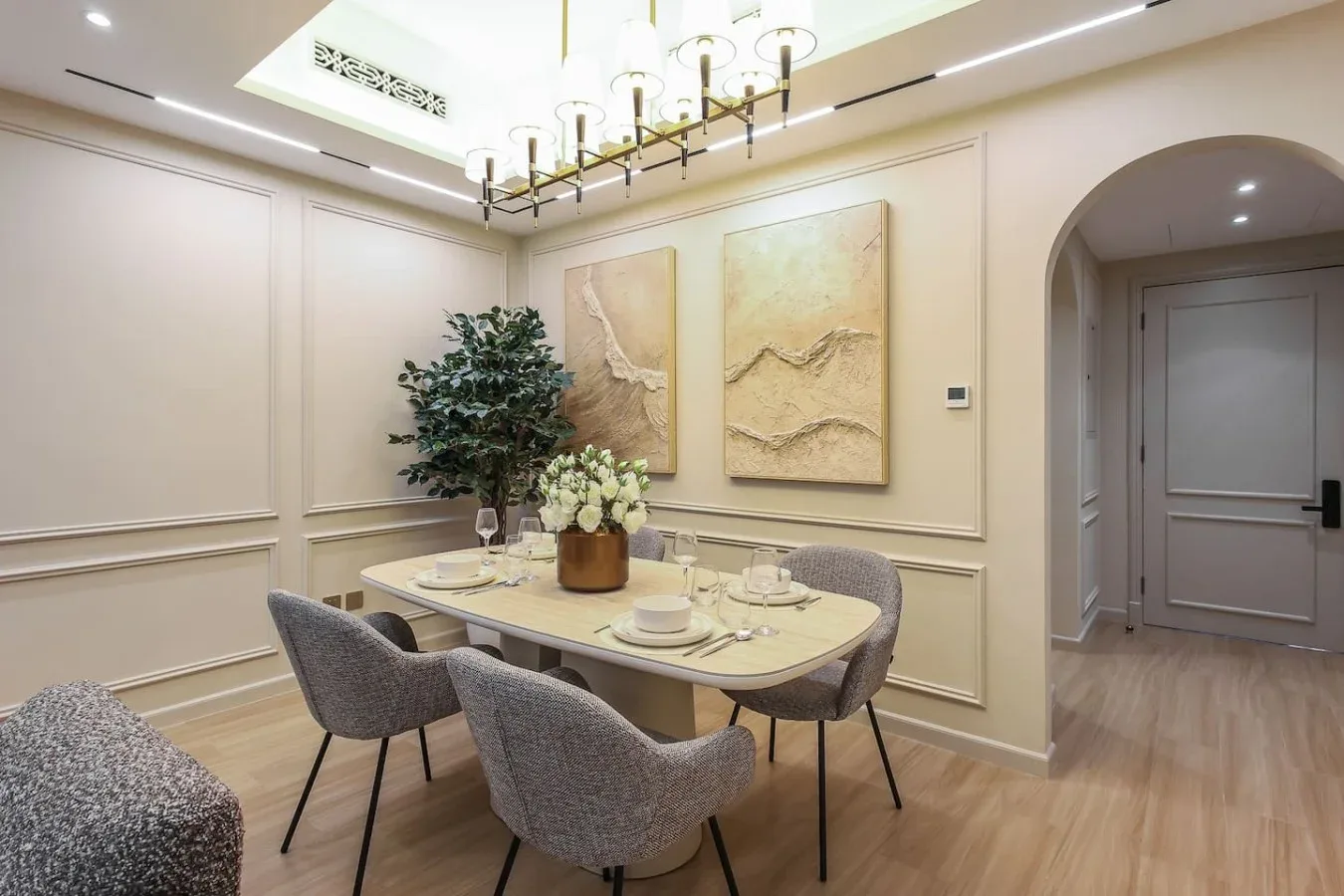 Comedor con la mesa puesta, asientos tapizados y cuadros en la pared.