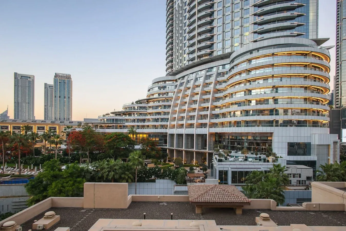 Un moderno edificio alto domina jardines y torres cercanas.