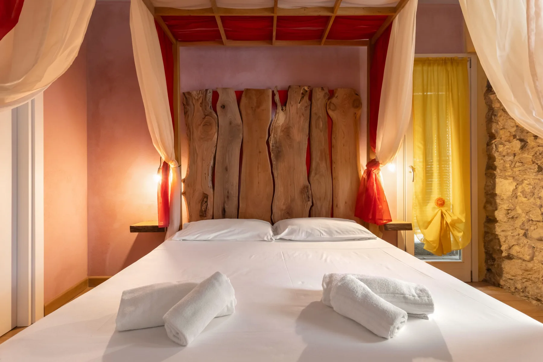 A bedroom with a white bed, rustic wooden headboard, and sheer curtains.