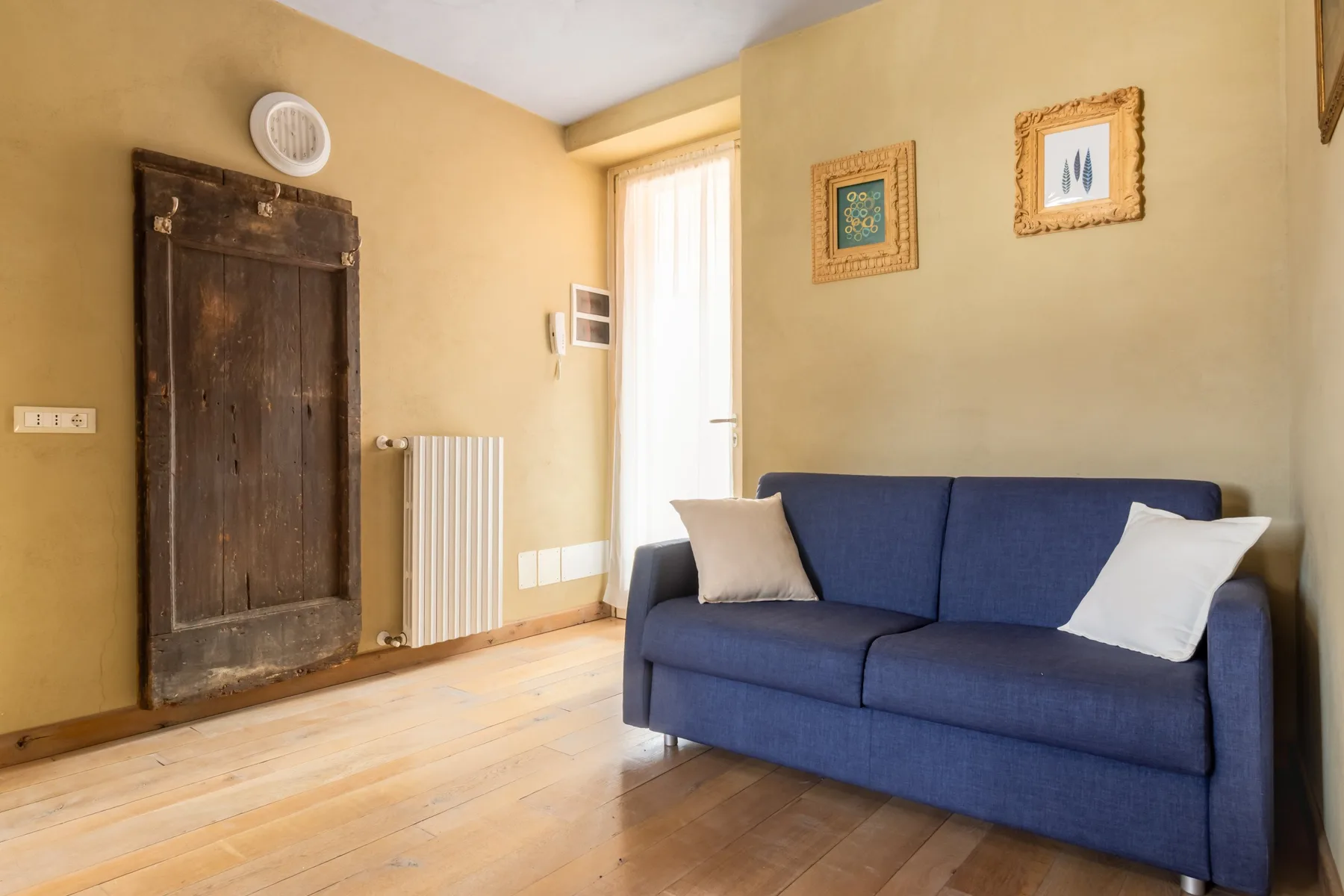 A living room with a blue sofa, framed pictures, and a bright window.