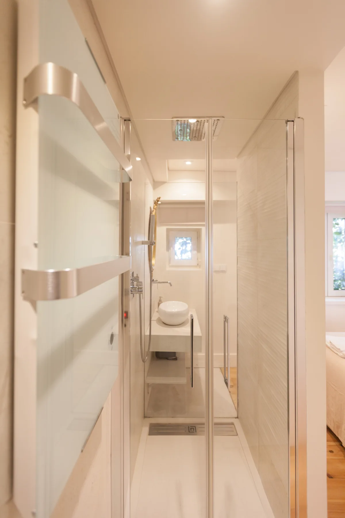 Zona de ducha en un baño con una mampara de vidrio y un lavabo al fondo.