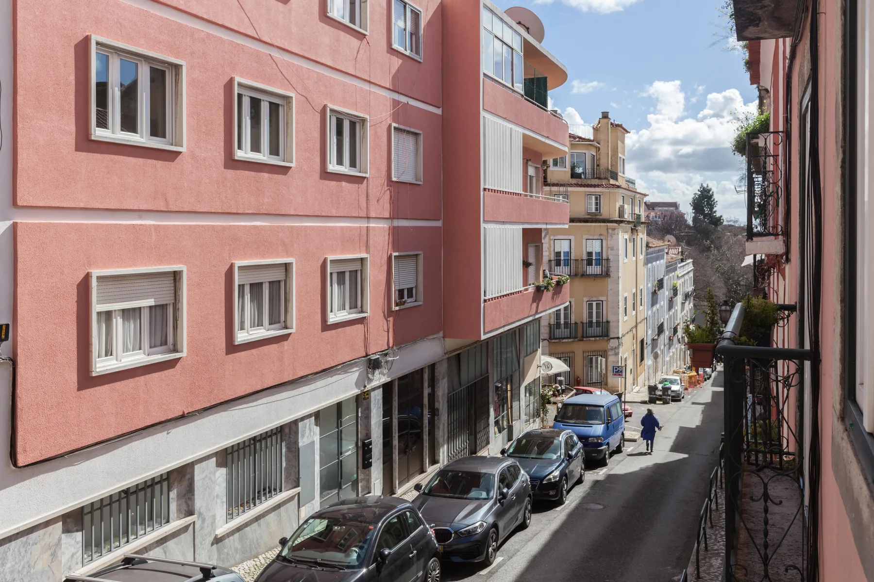 Una calle urbana estrecha bordeada de edificios de apartamentos de tonos pastel y coches aparcados.