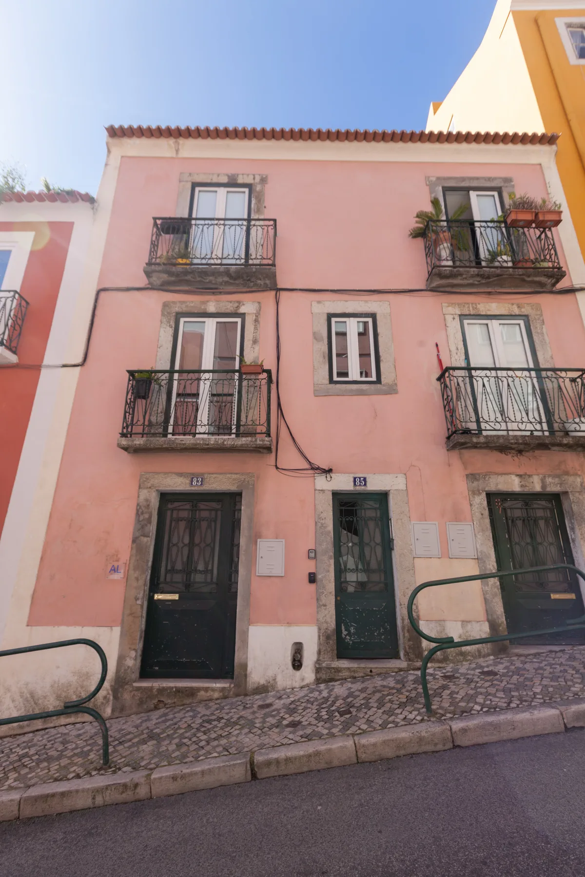 Edificio rosa con balcones y puertas oscuras a pie de calle.