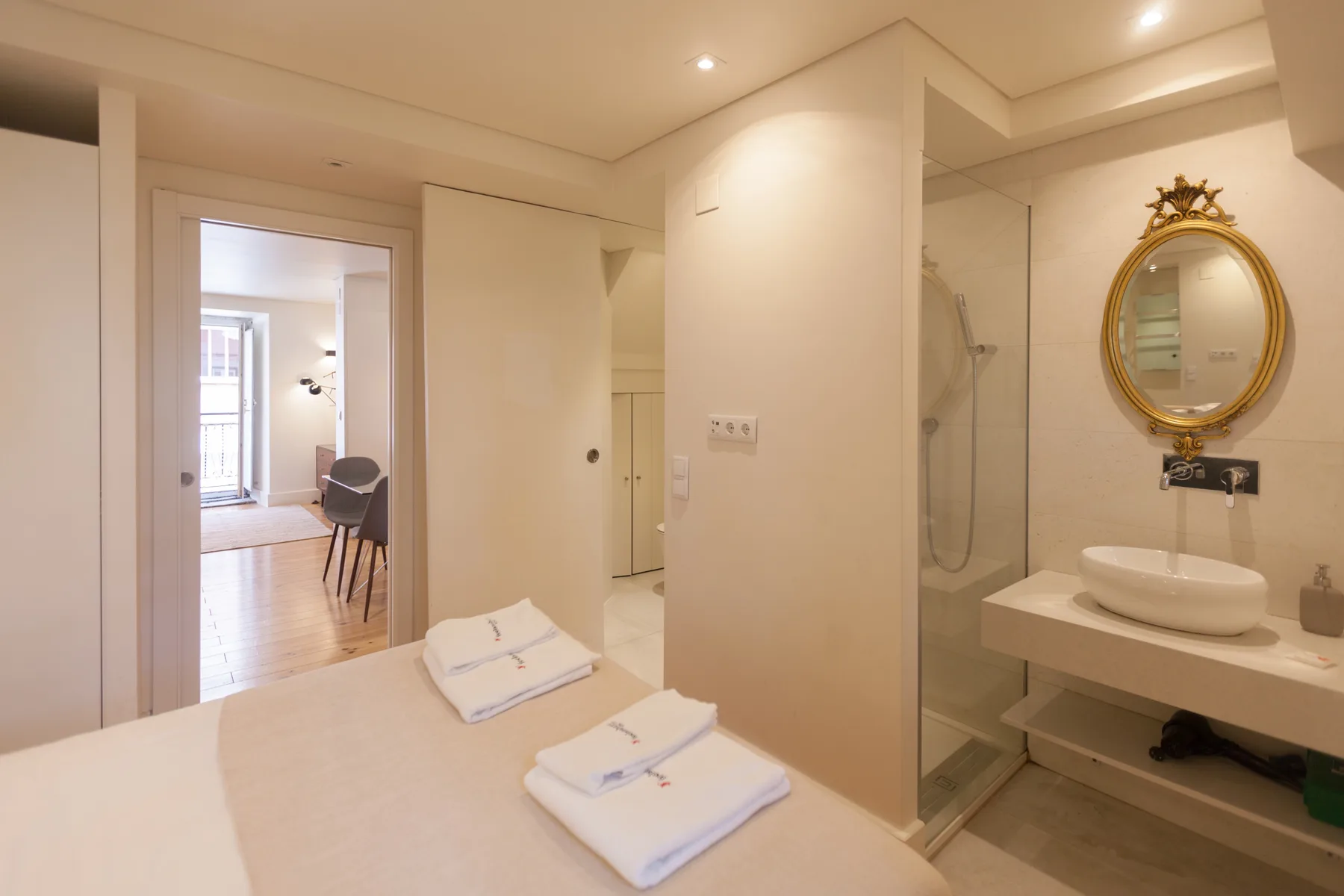 Un dormitorio luminoso da paso a un baño con ducha de cristal y lavabo.