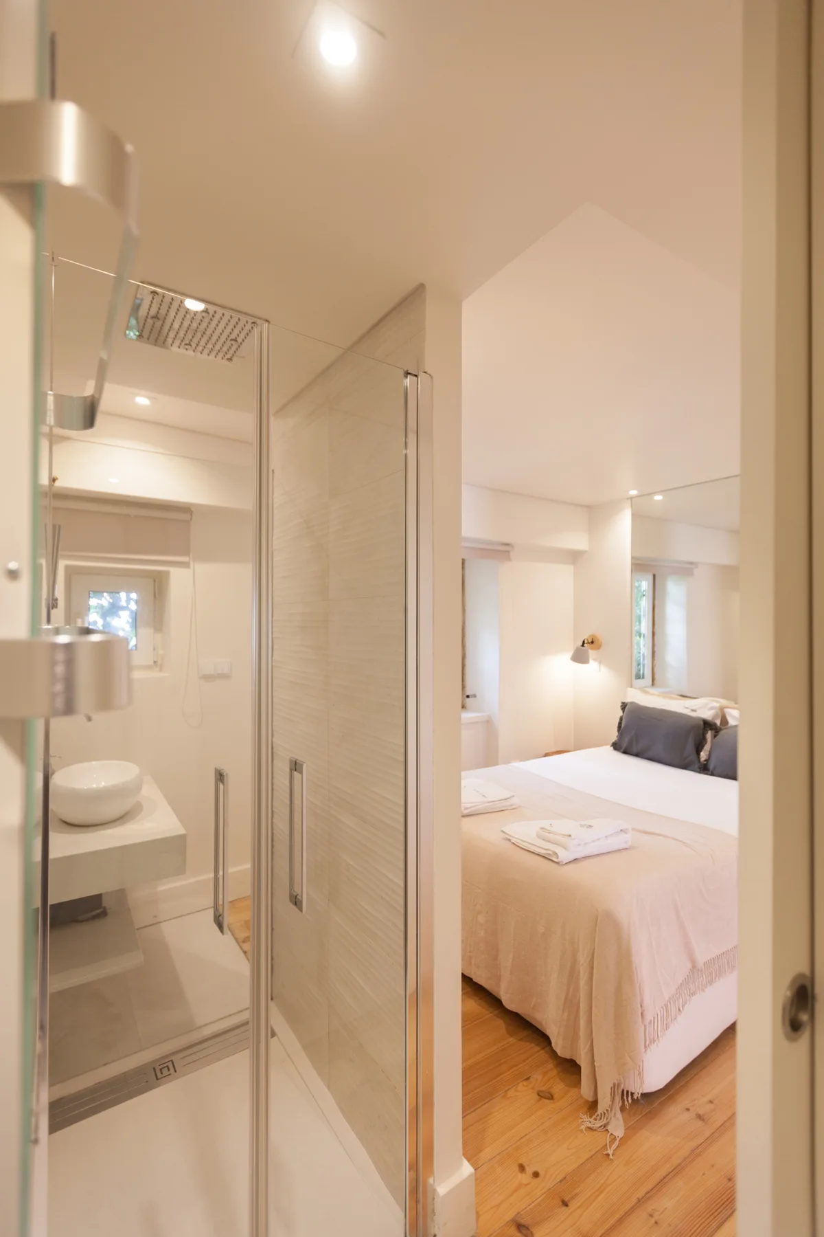 Se ve un dormitorio con una cama más allá de una ducha de vidrio.