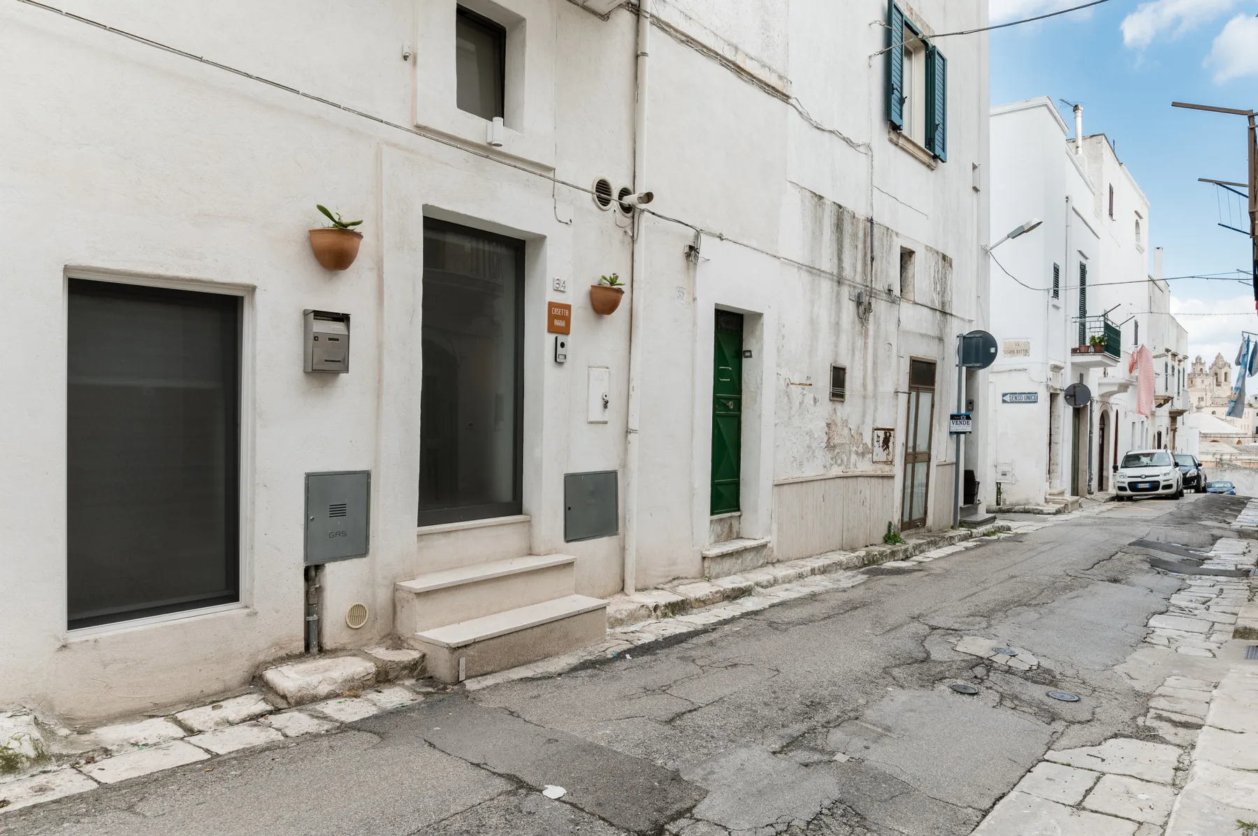 Una calle estrecha pavimentada, bordeada de edificios blancos y puertas oscuras.