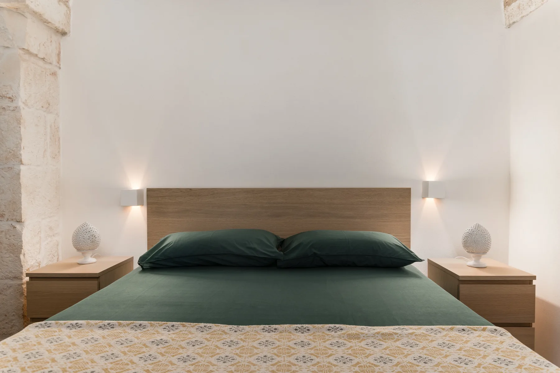Un dormitorio con una cama verde, cabecero de madera y mesitas a juego.