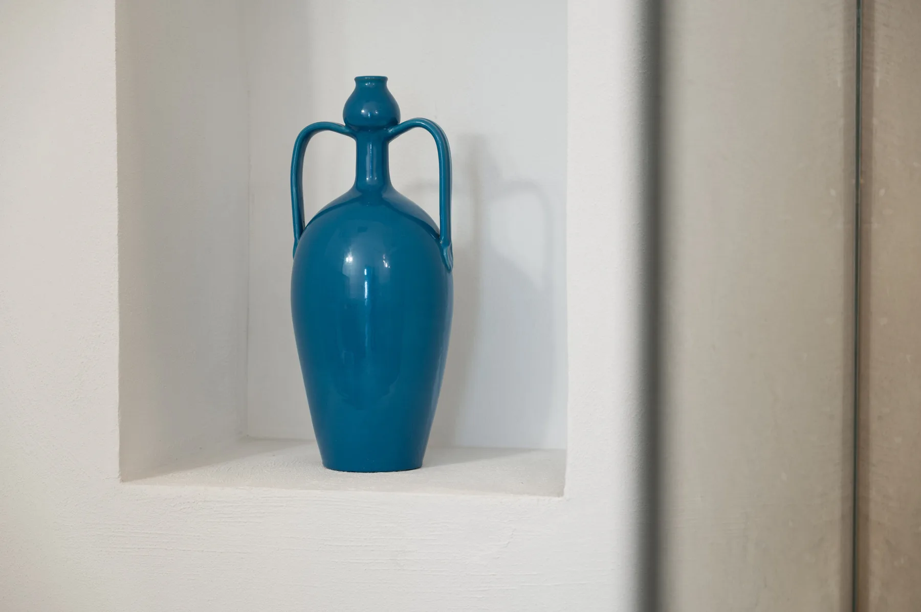 Un jarrón decorativo azul está en un nicho de pared.
