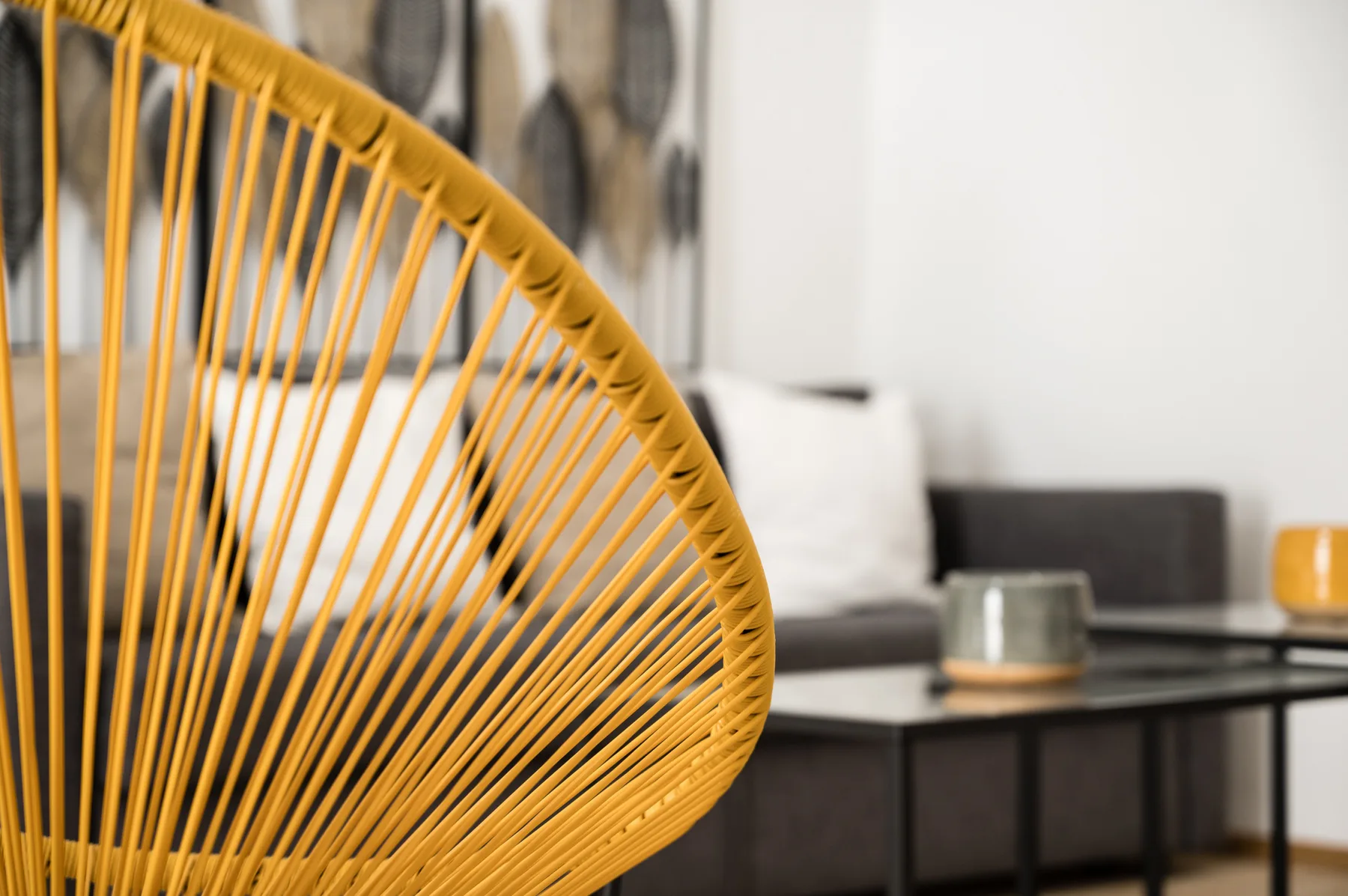 Un asiento tejido de color vivo ocupa el primer plano de una sala con sofá y mesa auxiliar.