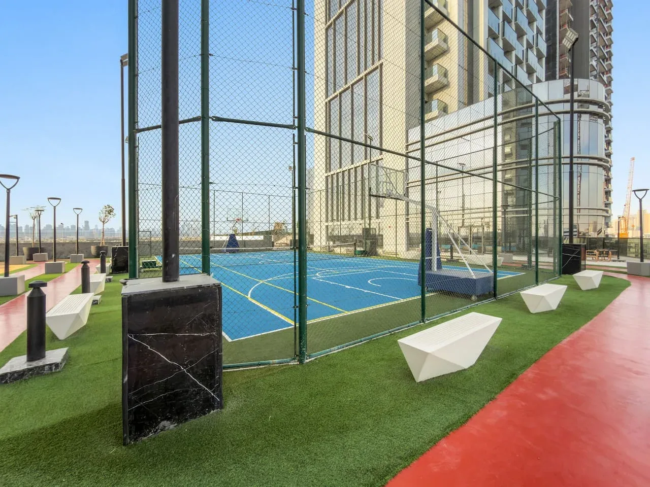 Una cancha deportiva al aire libre con superficies azules está junto a un edificio alto.