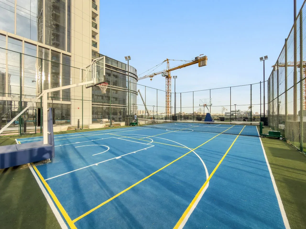 Una cancha de baloncesto azul al aire libre con líneas pintadas junto a un edificio alto.
