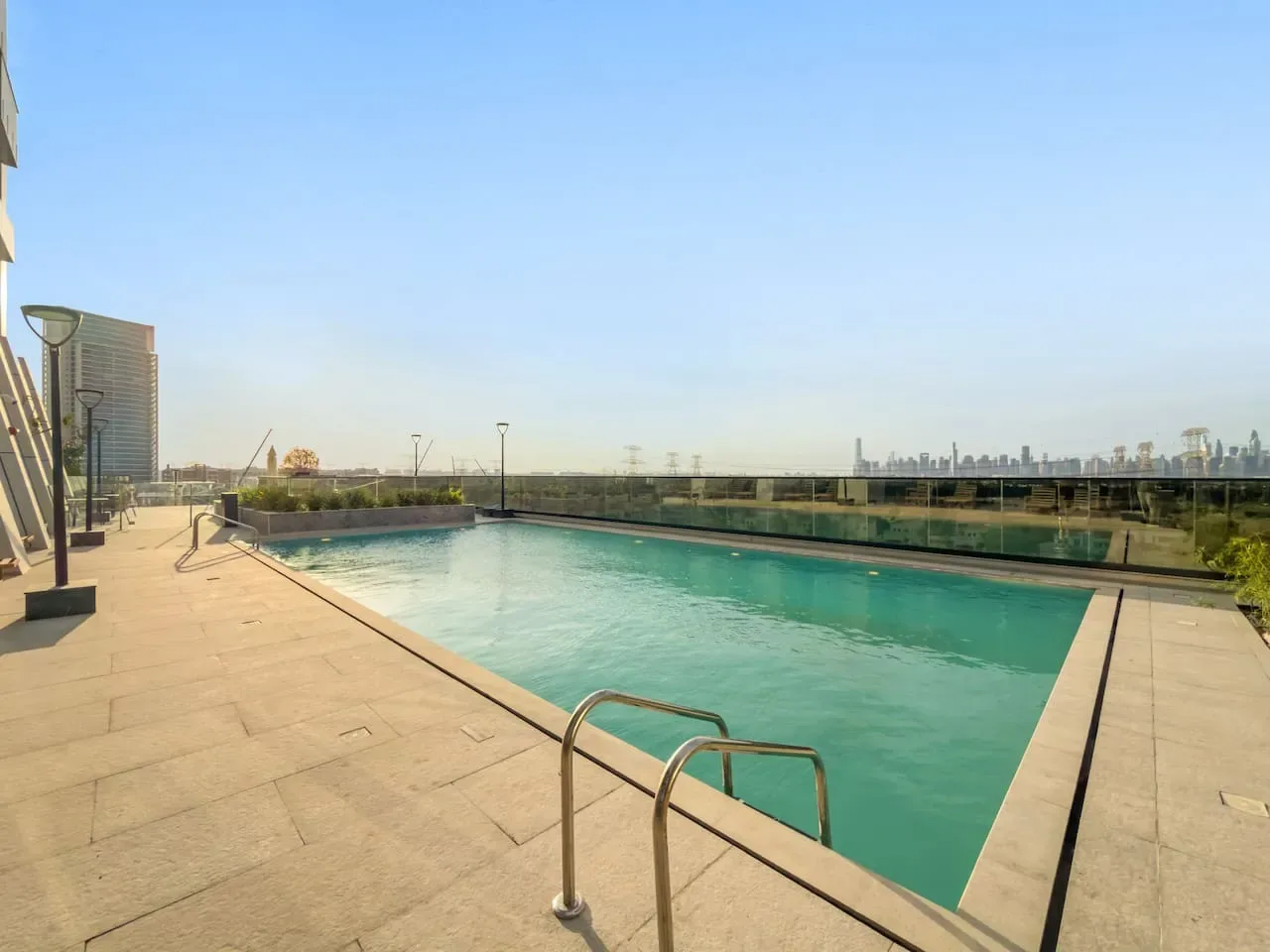 Una piscina al aire libre está junto a una amplia terraza pavimentada bajo un cielo despejado.