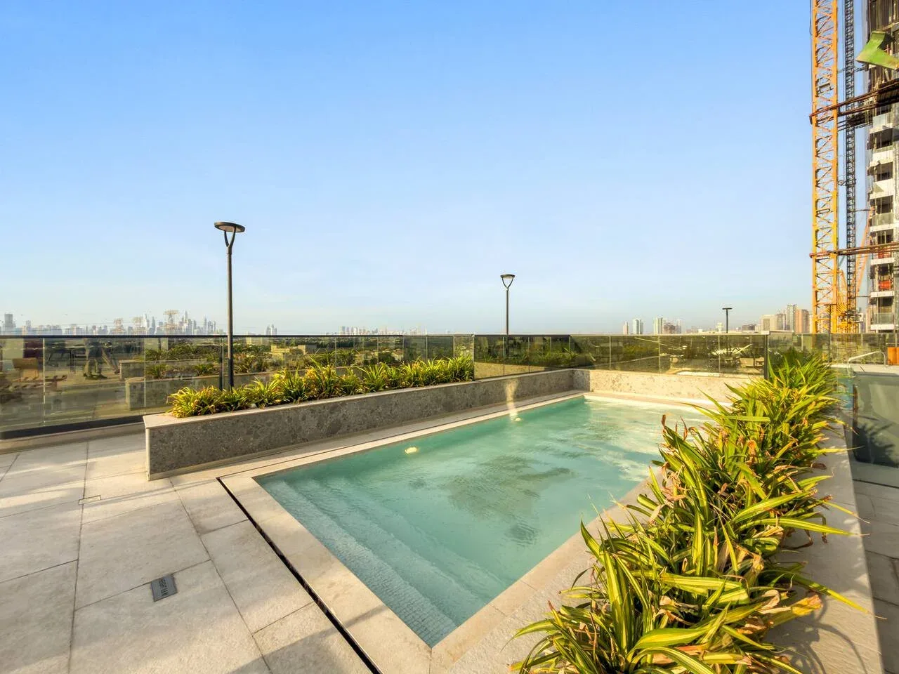 Una piscina en la azotea está junto a jardineras, con edificios de la ciudad a lo lejos.