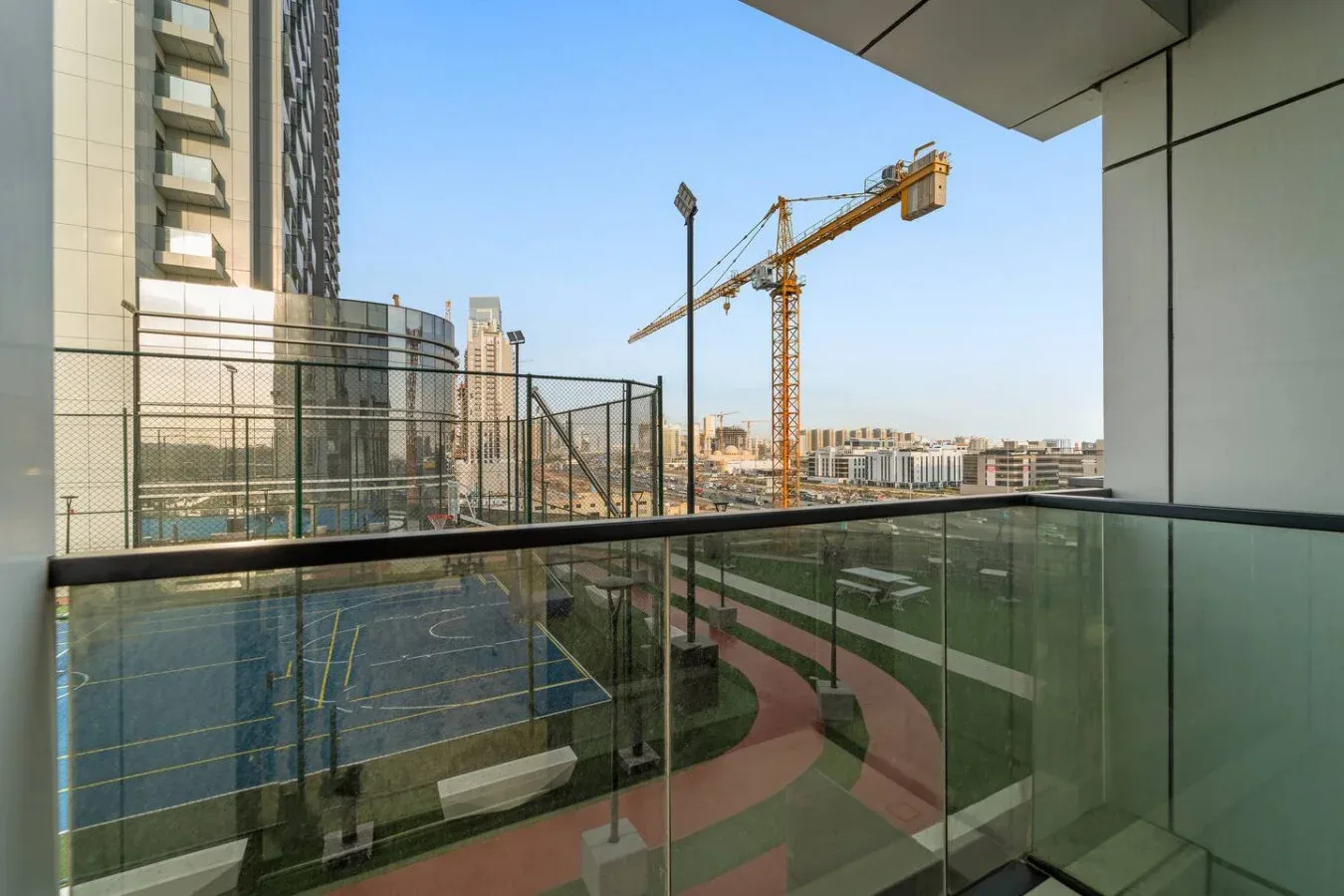 Un balcón da a unas canchas deportivas cercadas, una pista para correr y obras cercanas.