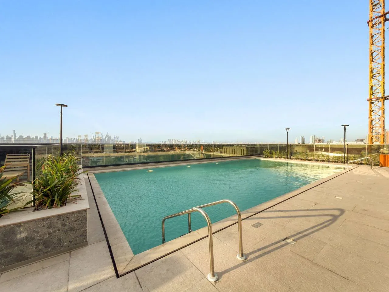 Una piscina al aire libre está rodeada por una terraza pavimentada, con el perfil urbano al fondo.