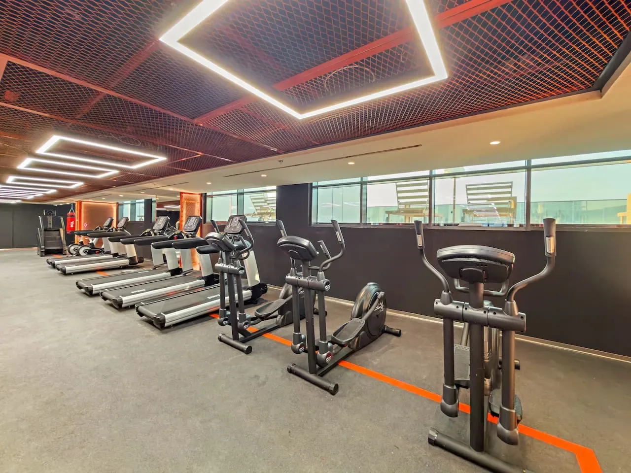 Un gimnasio con máquinas de ejercicio cardiovascular bajo luces geométricas en el techo.