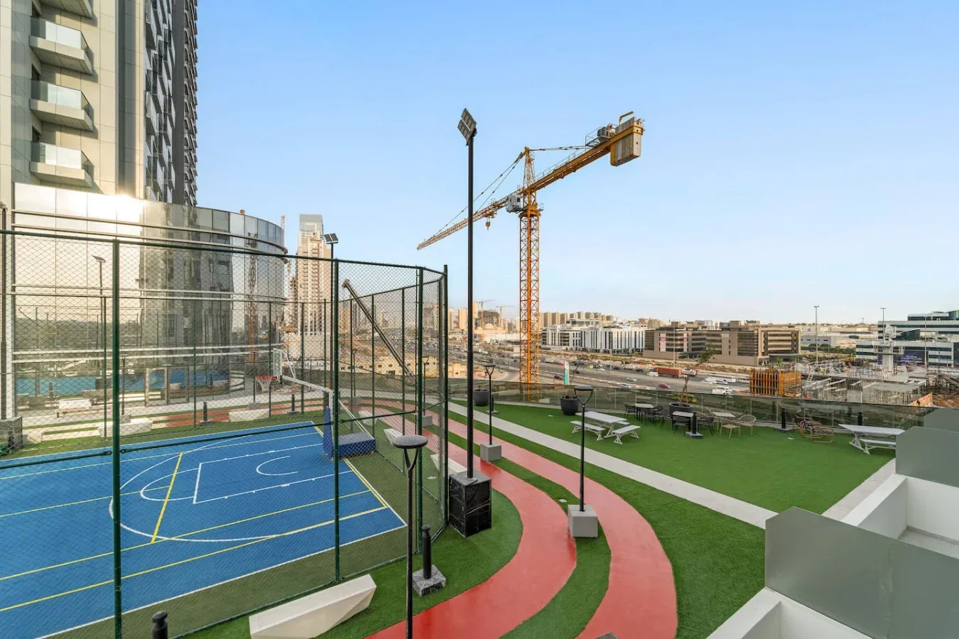 Zona deportiva exterior con una cancha cercada, pista para correr y edificios alrededor.