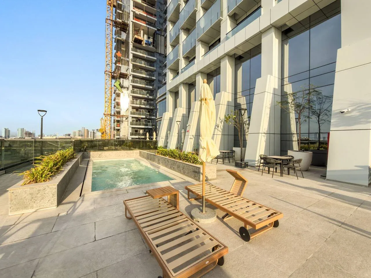 Zona de piscina al aire libre junto a un edificio moderno, con tumbonas en la terraza pavimentada.