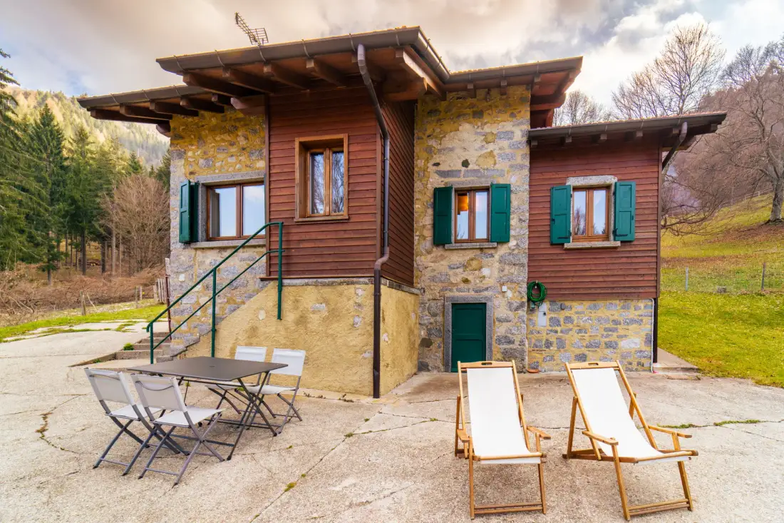 A stone-and-wood house stands beside a paved patio with outdoor seating.