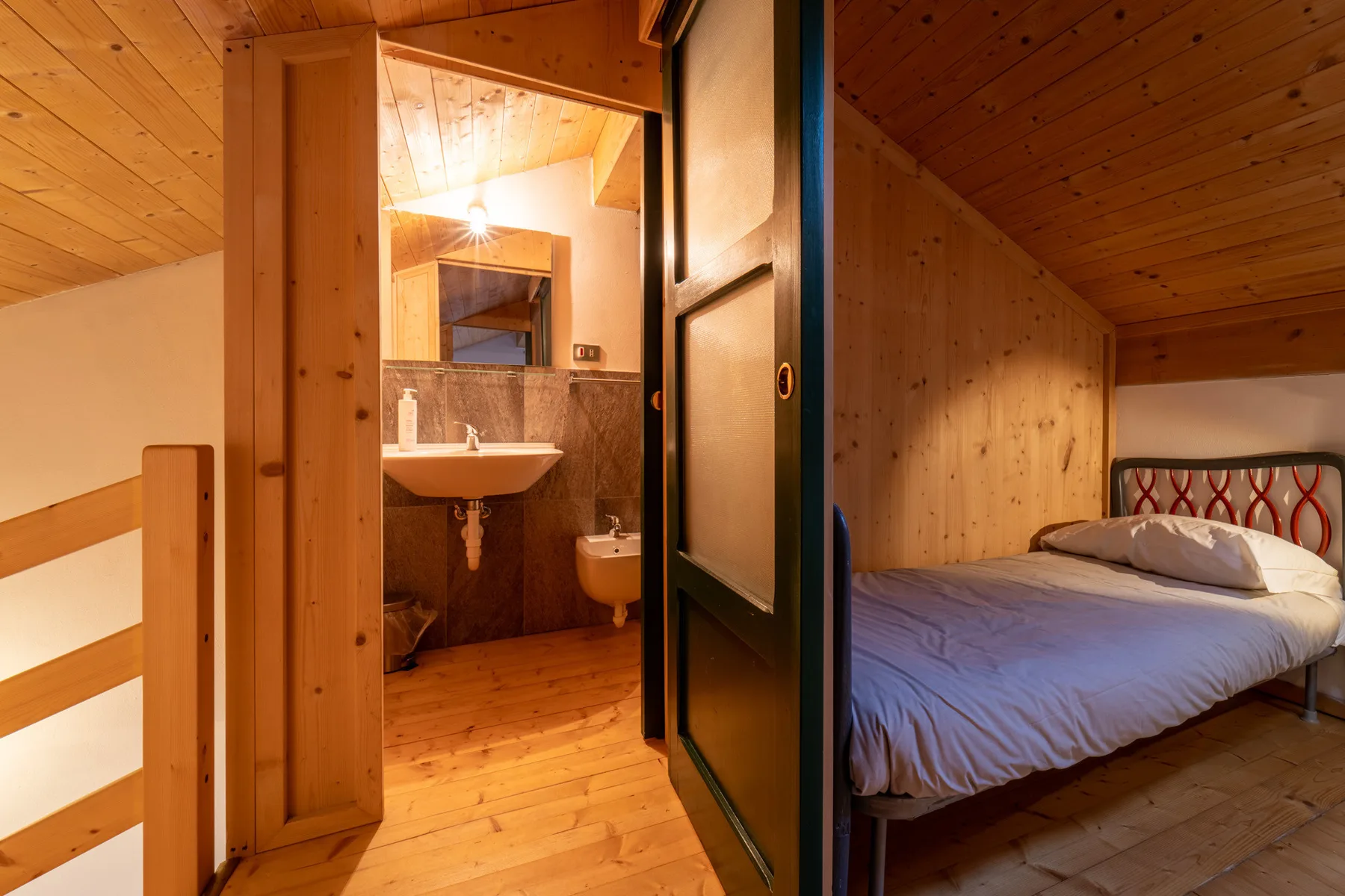 A wood-paneled bedroom with a bed beside an open bathroom doorway.