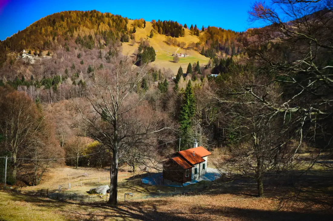 A small cabin with an orange roof sits in a wooded mountain valley.