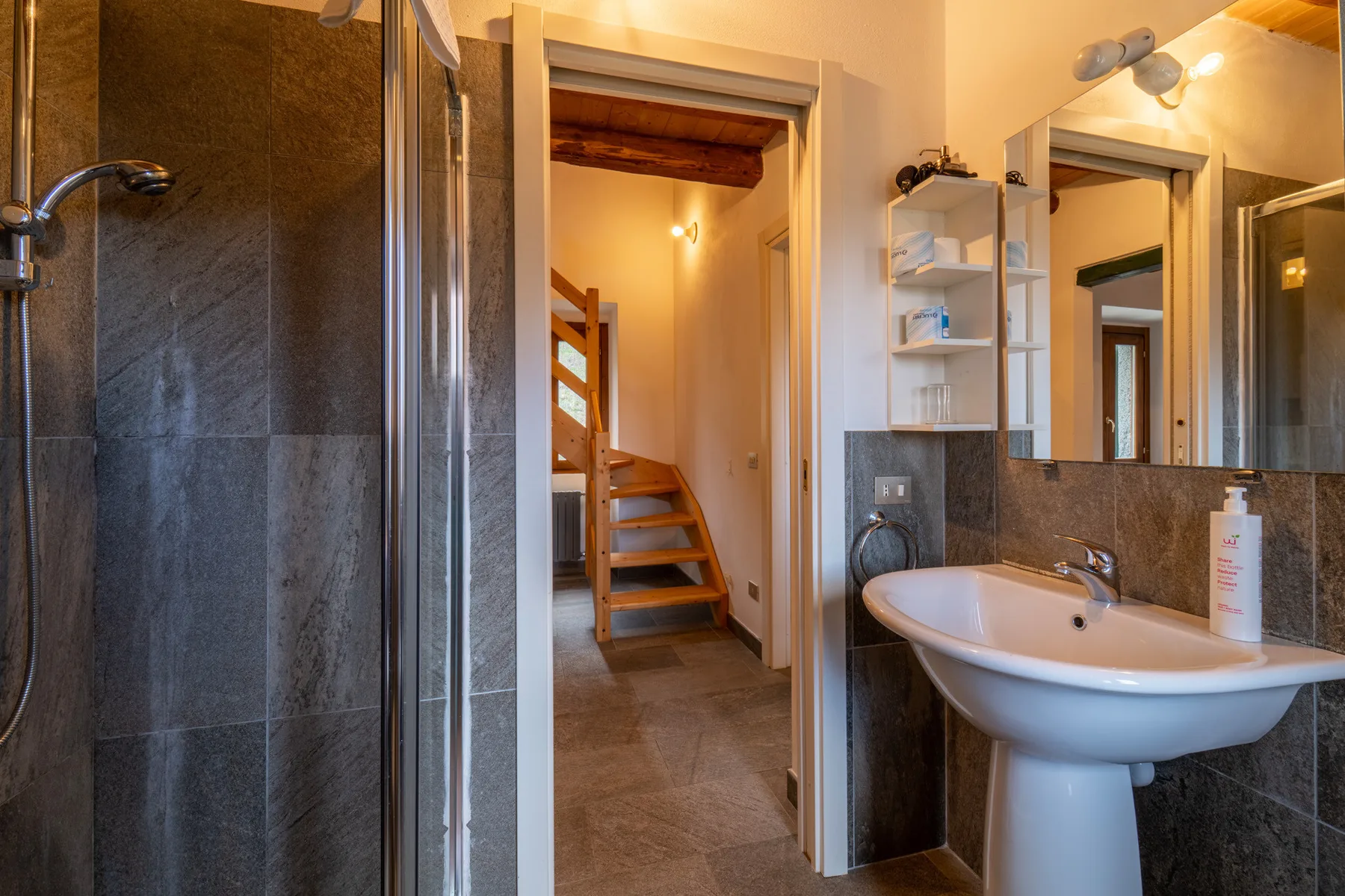 A bathroom with a sink and shower, opening onto a hallway with stairs.