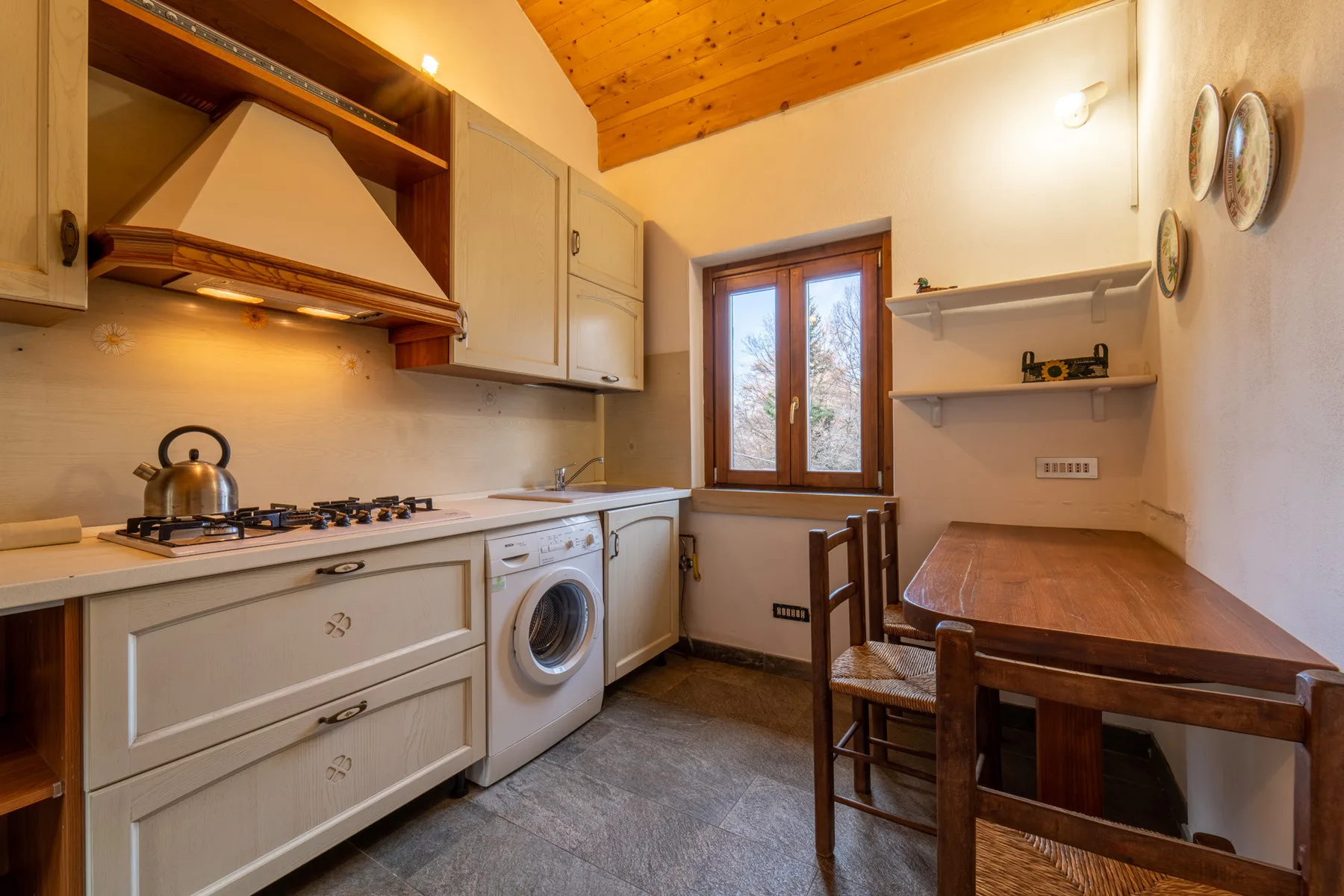 A compact kitchen and dining area with a wooden table beside the window.