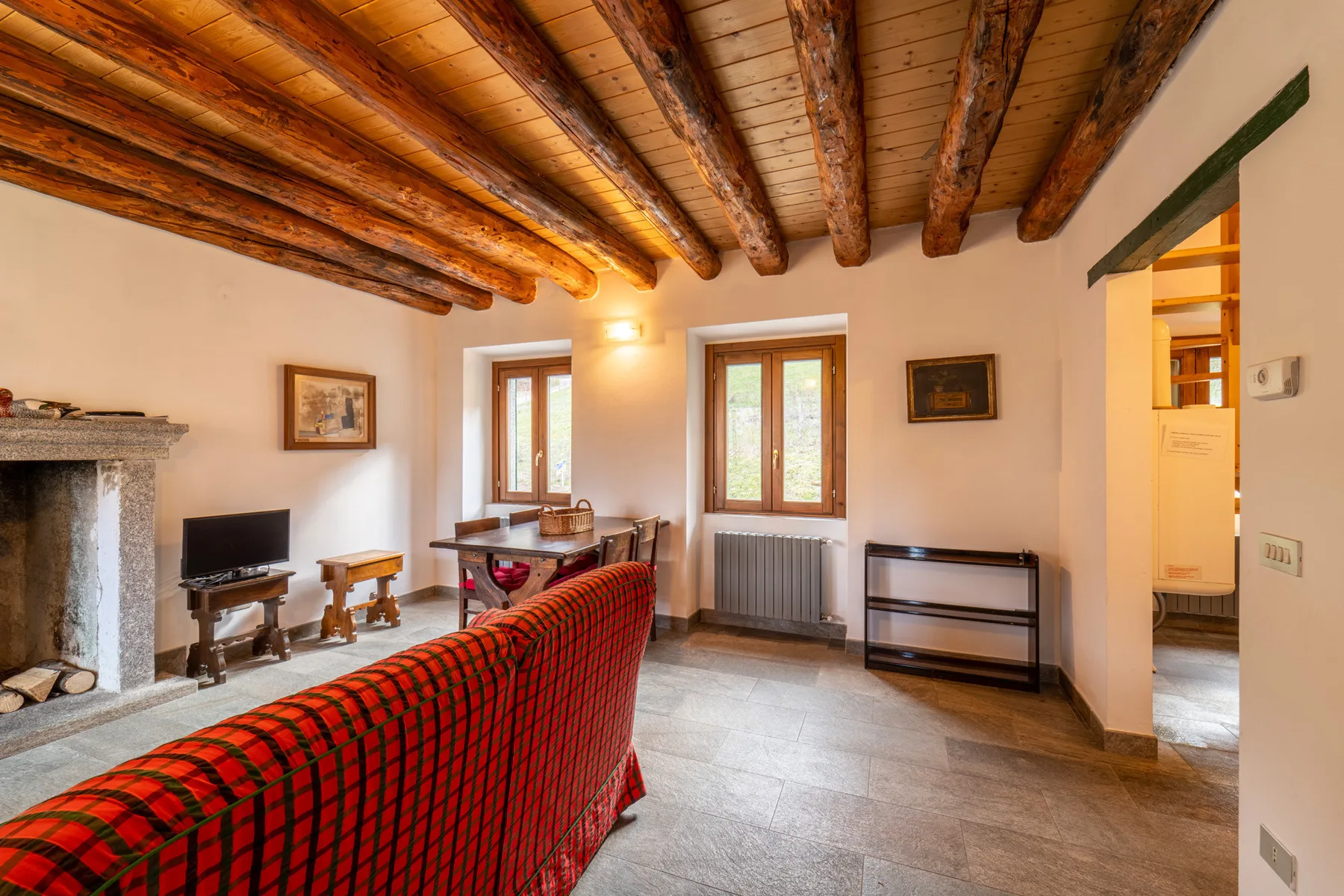 Living room with a red plaid sofa, exposed wooden ceiling beams, and windows.