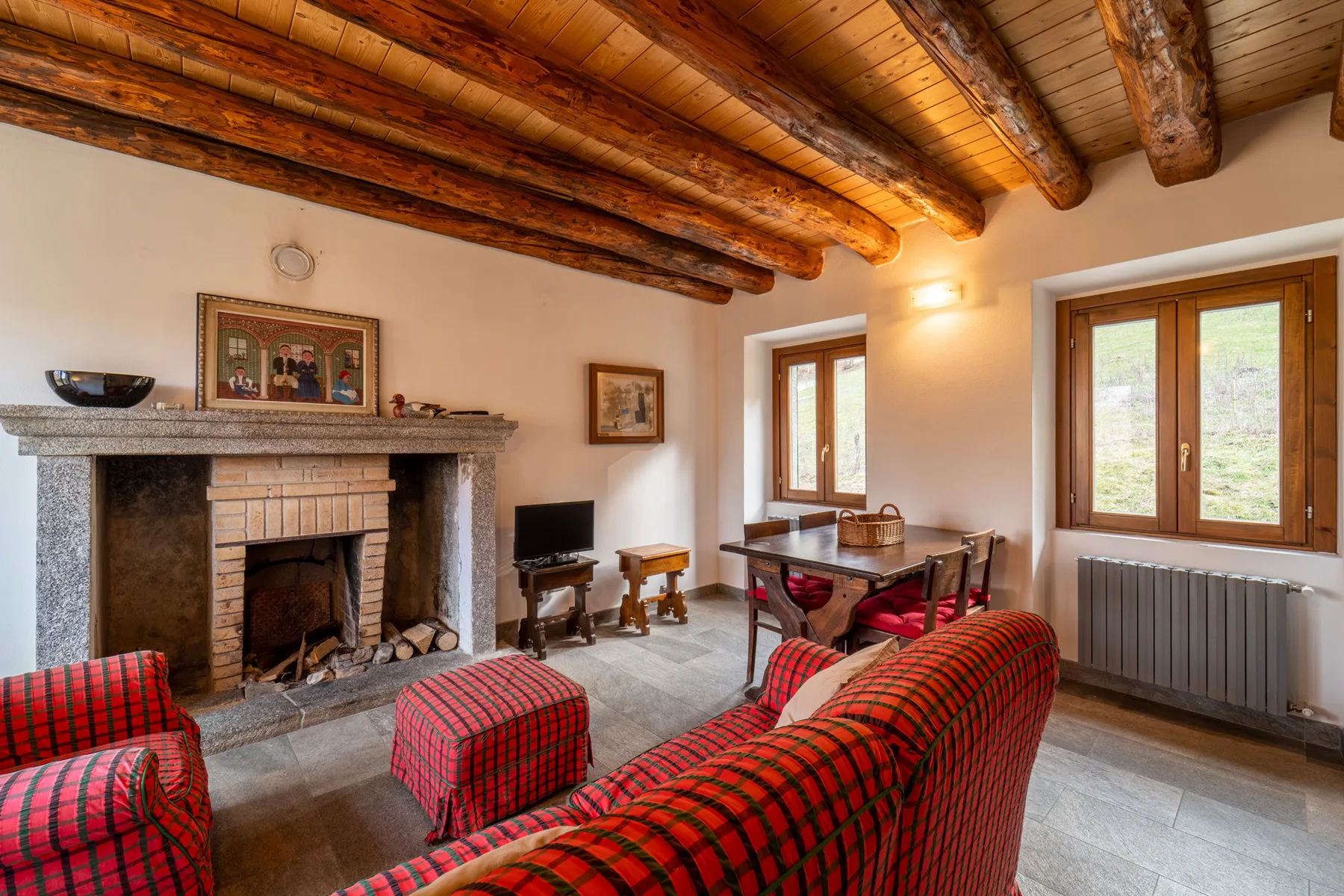 A living room with exposed wooden ceiling beams and a stone fireplace.
