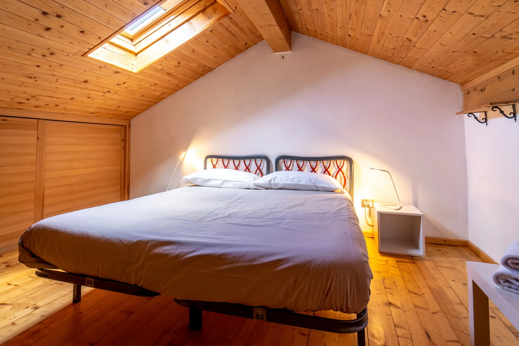A bedroom with a large bed beneath a sloped wooden ceiling and skylight.
