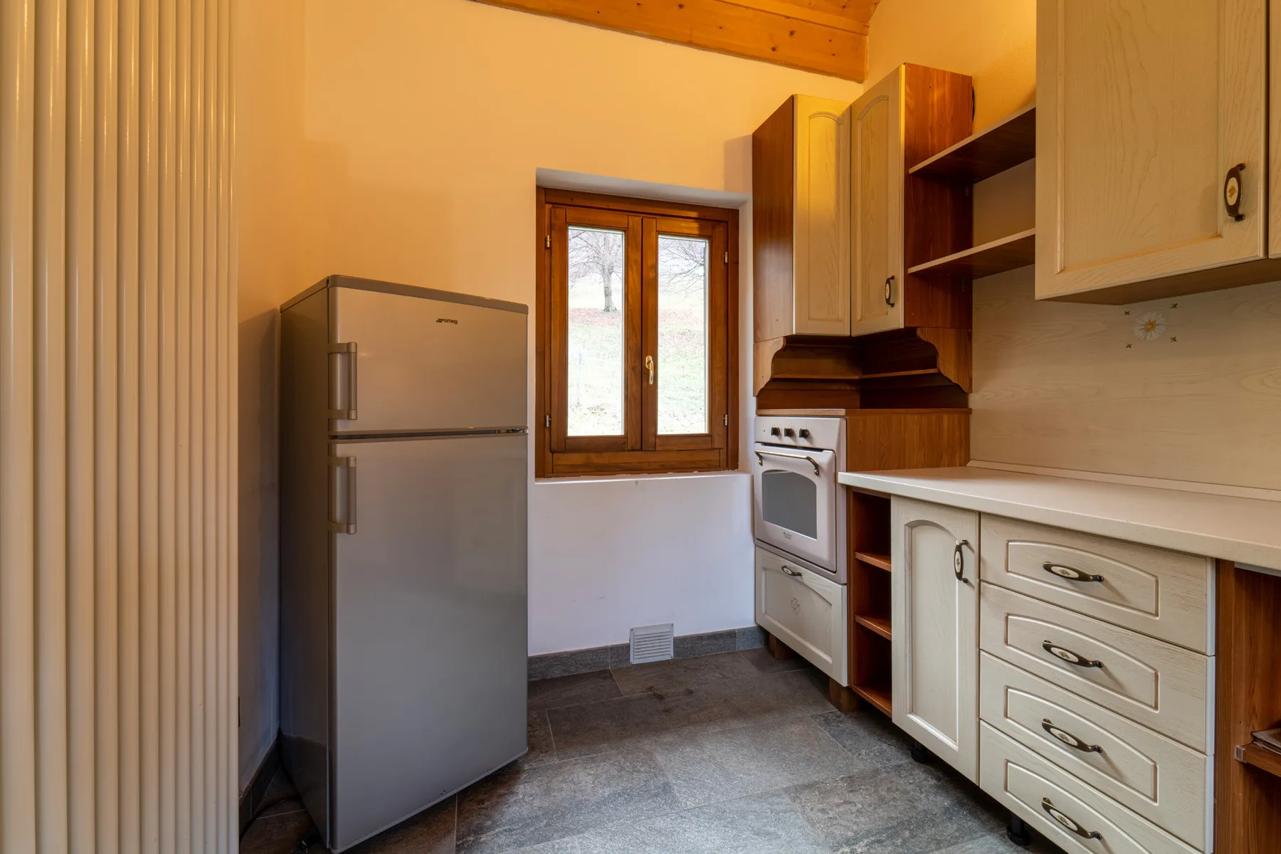A compact kitchen with a refrigerator, oven, and window.