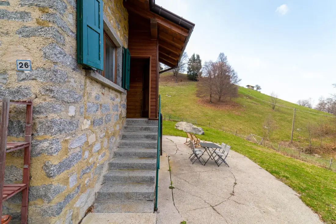 A stone building entrance opens onto a paved patio with outdoor seating.