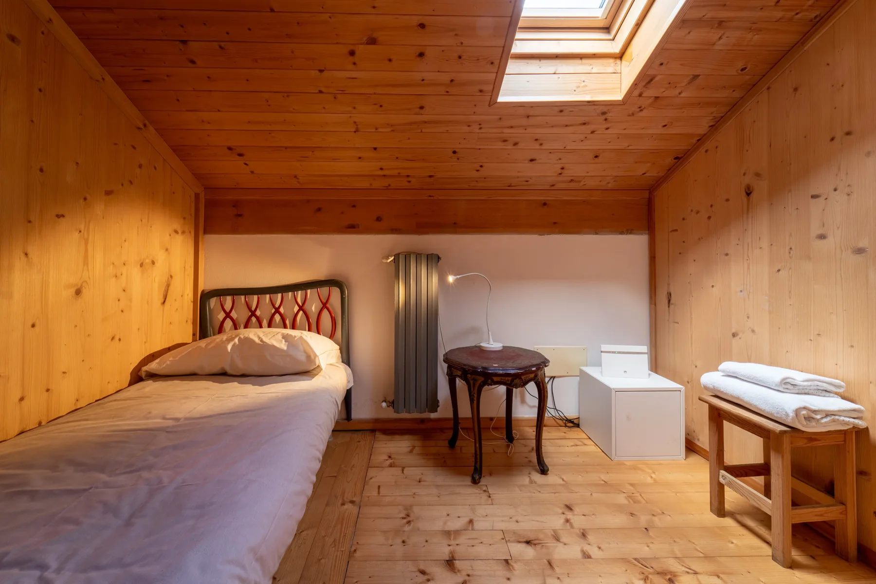 A wood-paneled bedroom with a bed, a small table, and a skylight.