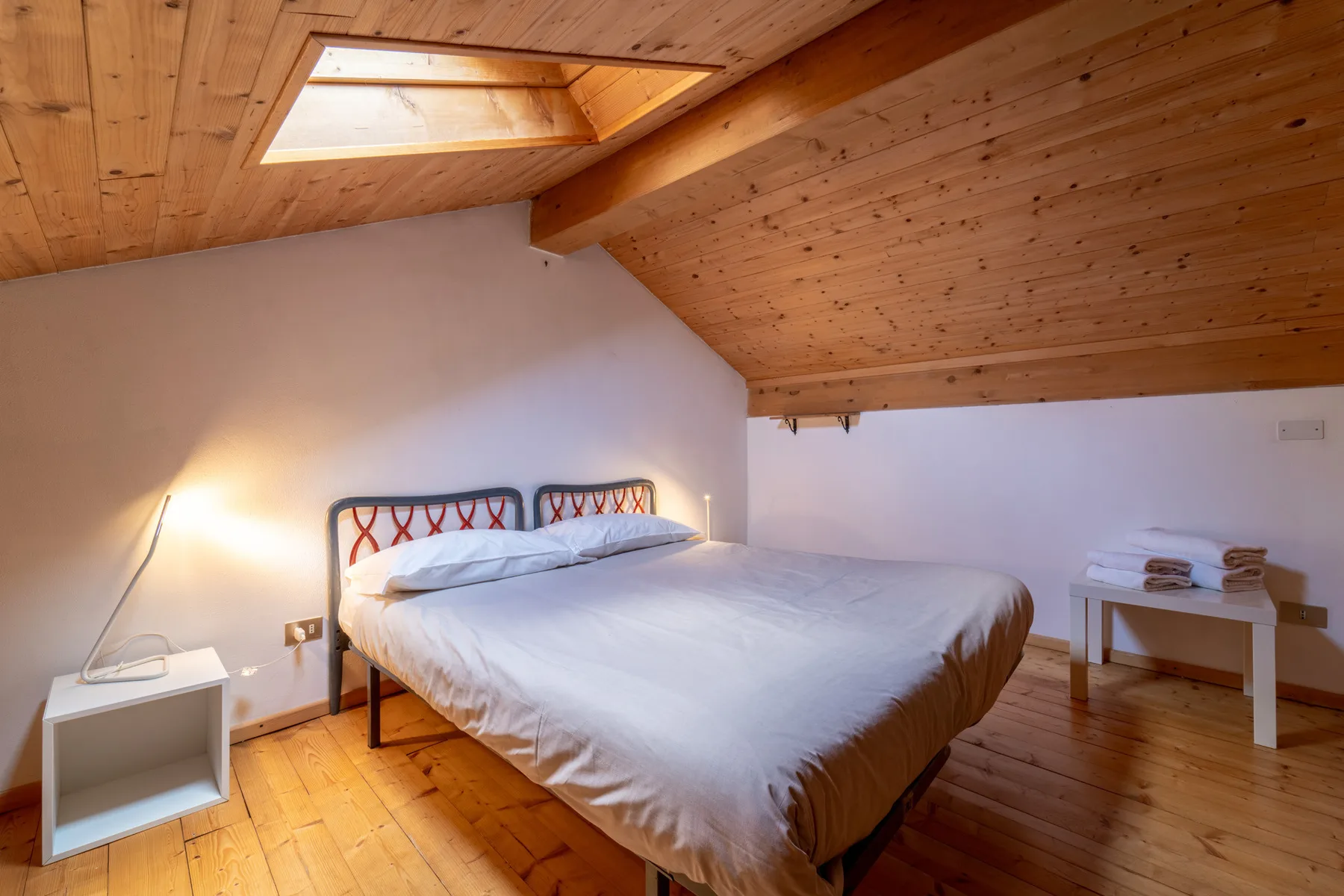 A bedroom with a bed beneath a sloped wooden ceiling and skylight.