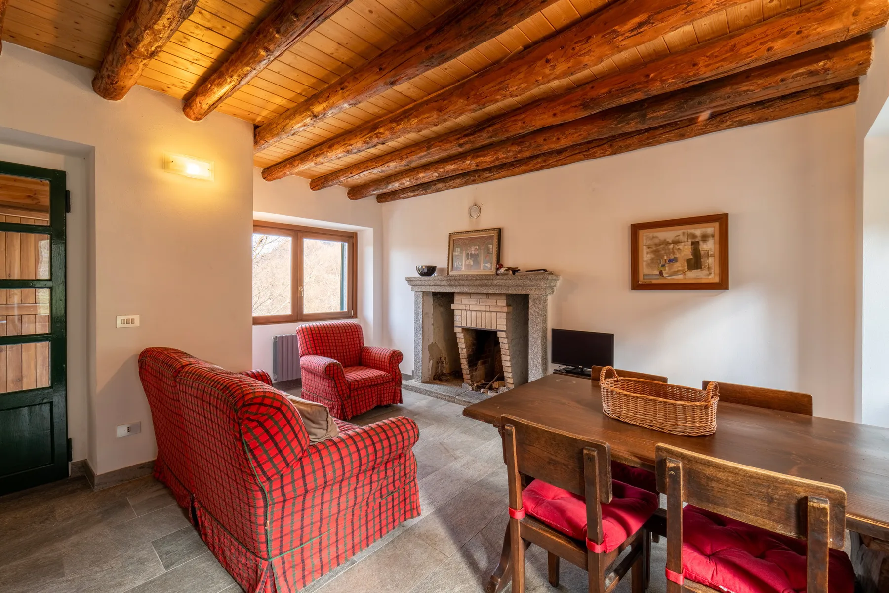 A living and dining room with red seating, a fireplace, and a wooden table.
