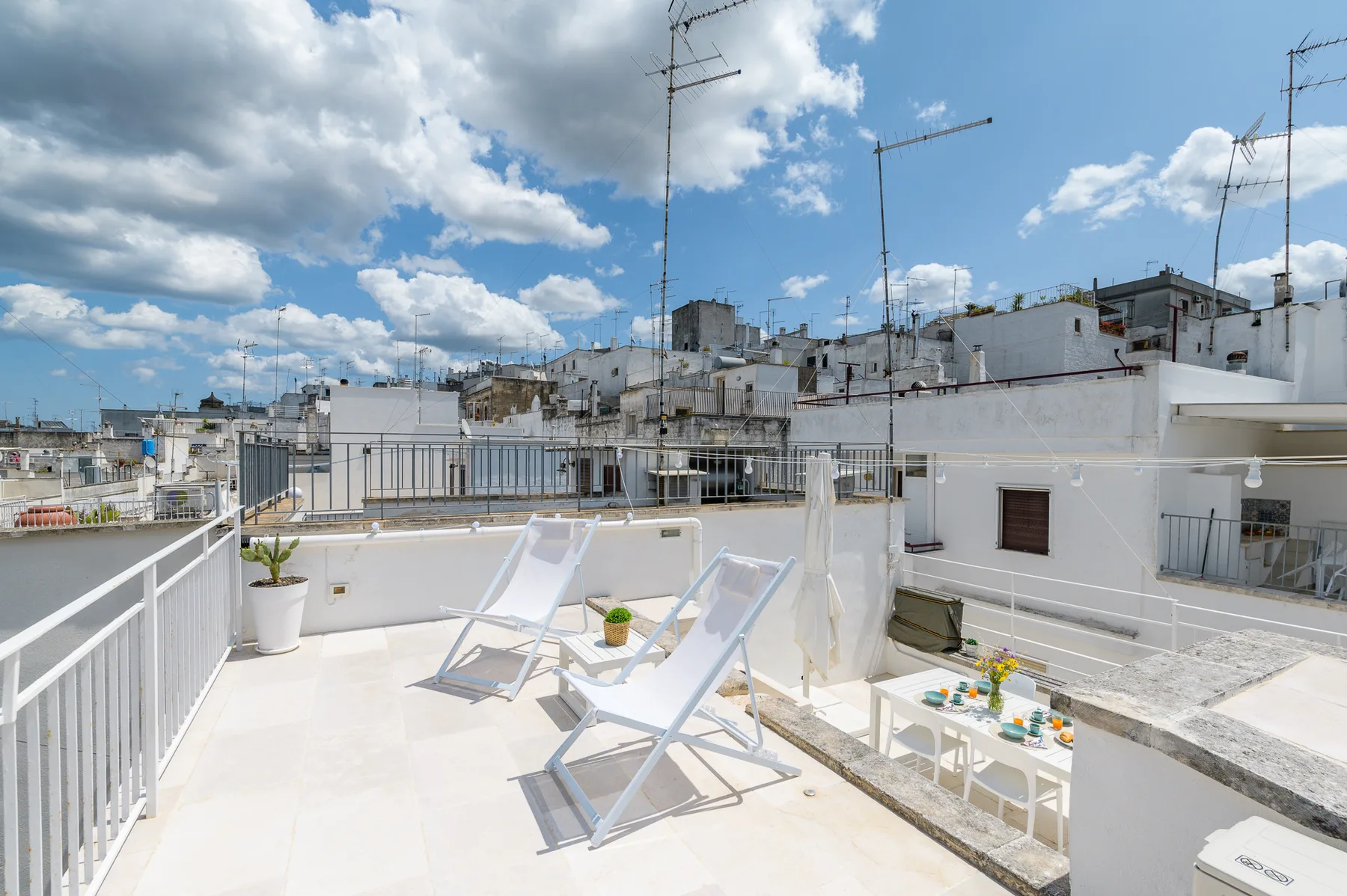 A sunny rooftop terrace with white lounge chairs and surrounding buildings.