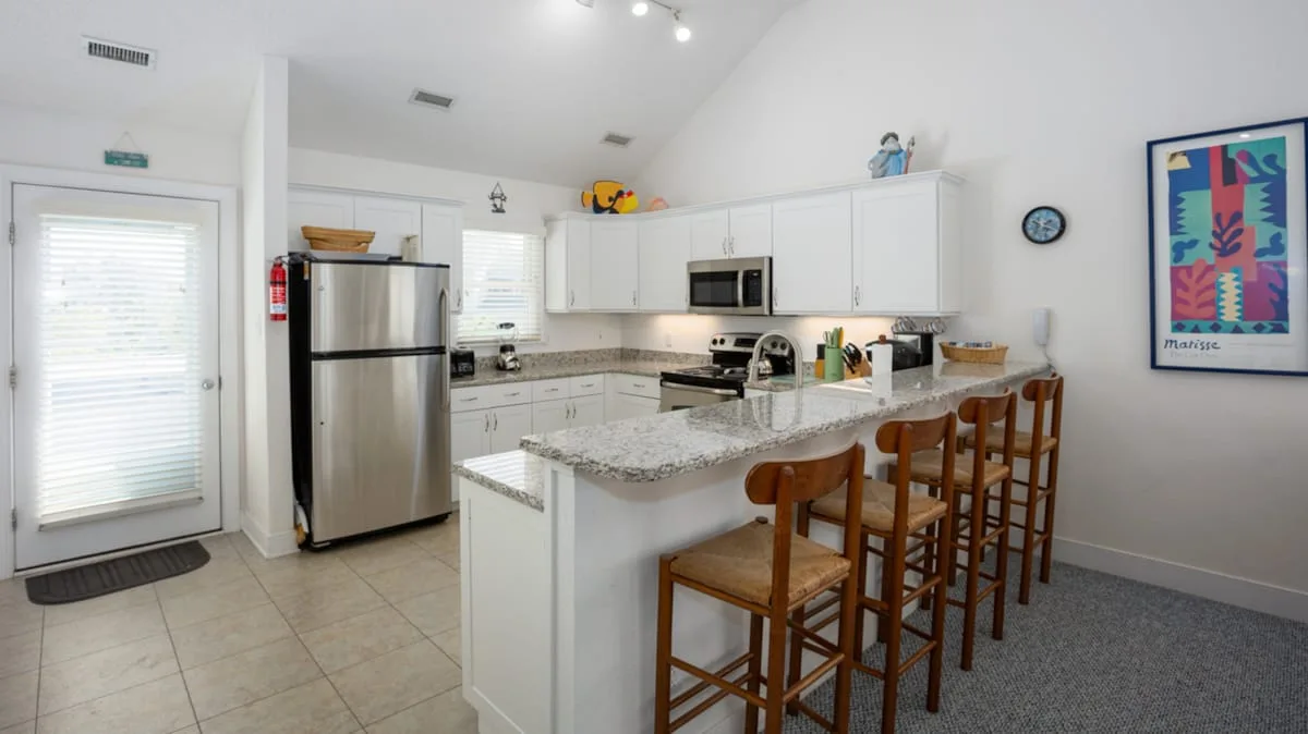 Una cocina luminosa con gabinetes blancos, electrodomésticos de acero inoxidable y una barra.