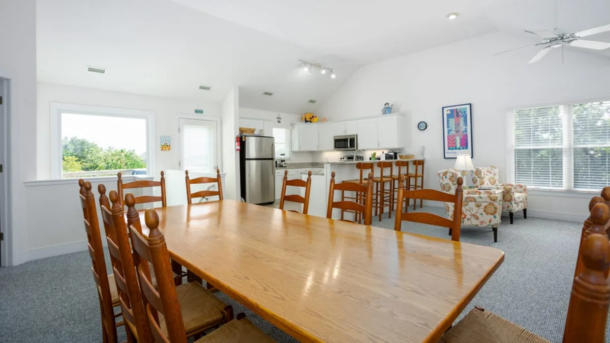 Un comedor luminoso con una mesa grande de madera y una cocina contigua.