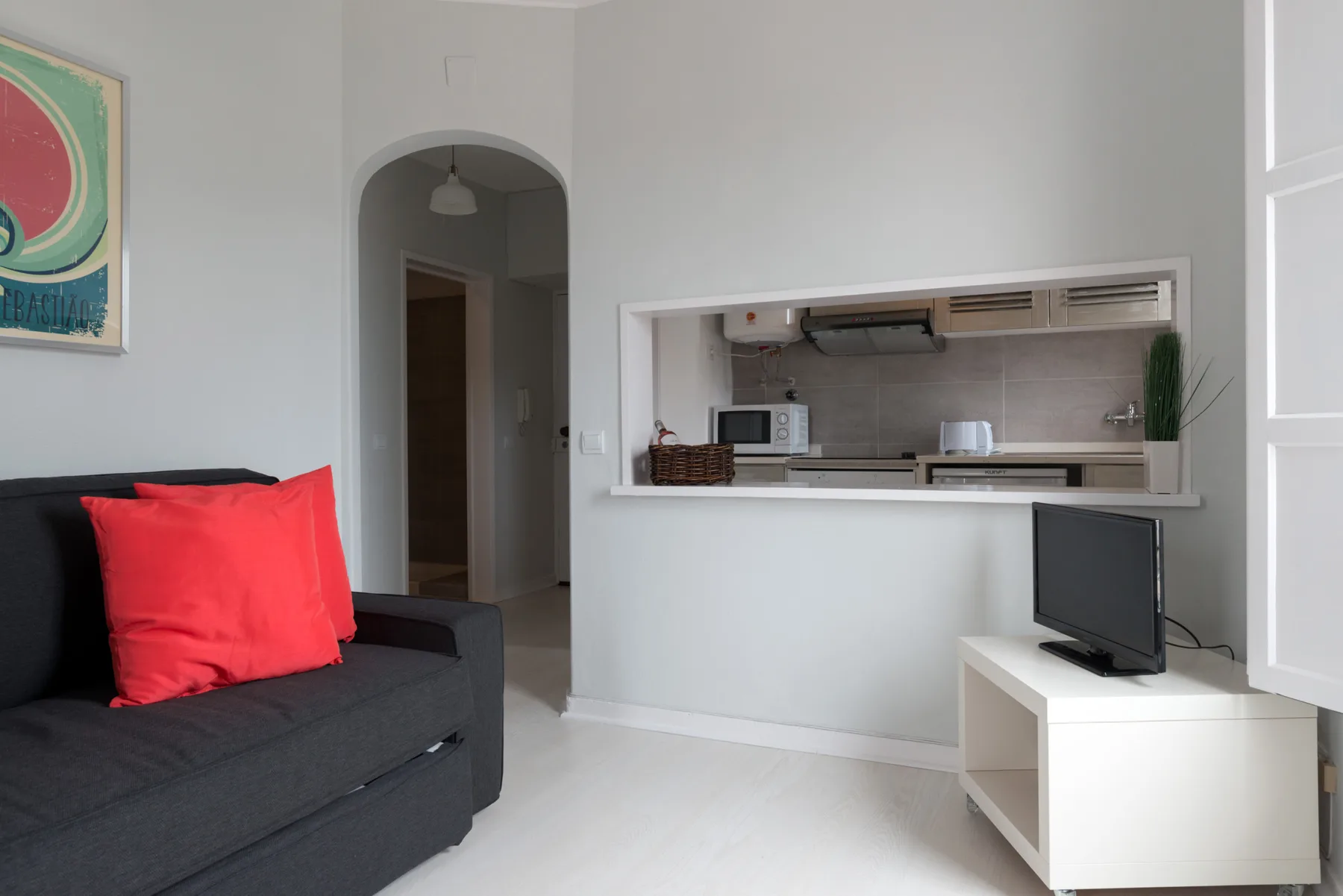 Una sala de estar con asientos oscuros y una cocina visible a través de una abertura.