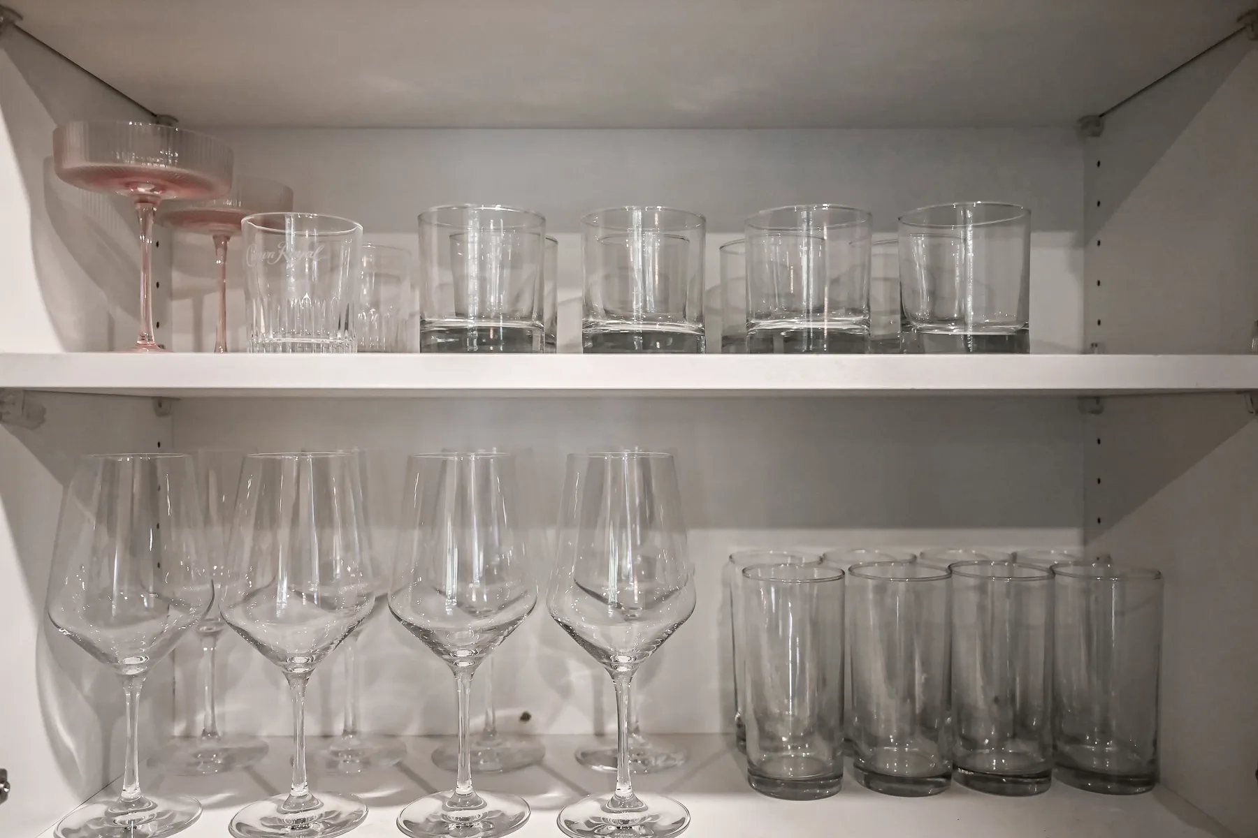 A cupboard shelf holds drinking glasses and wine glasses.