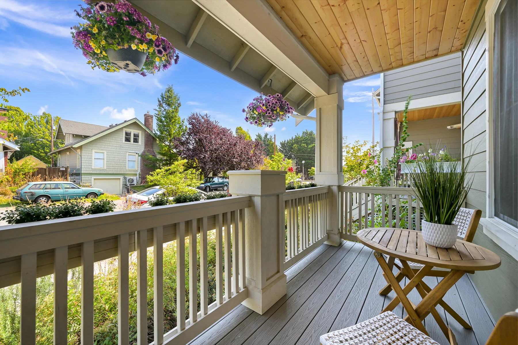 A covered porch with railing, a small table, and hanging flower baskets.