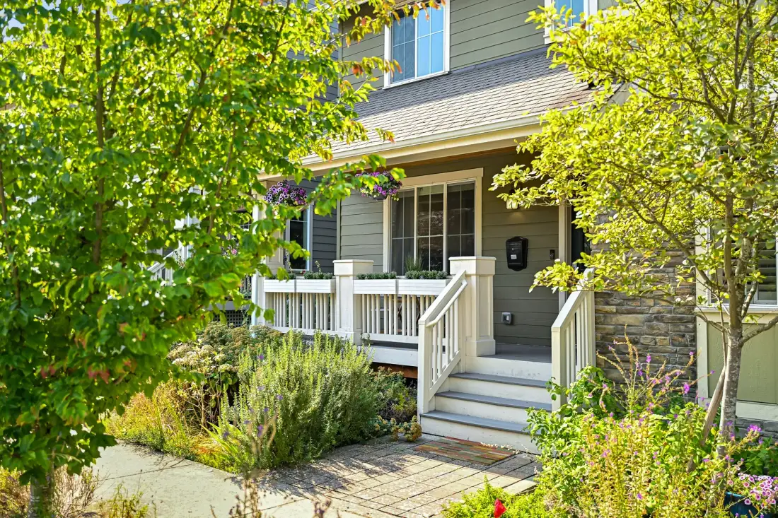 A house entrance with white steps and a small covered porch amid leafy landscaping.