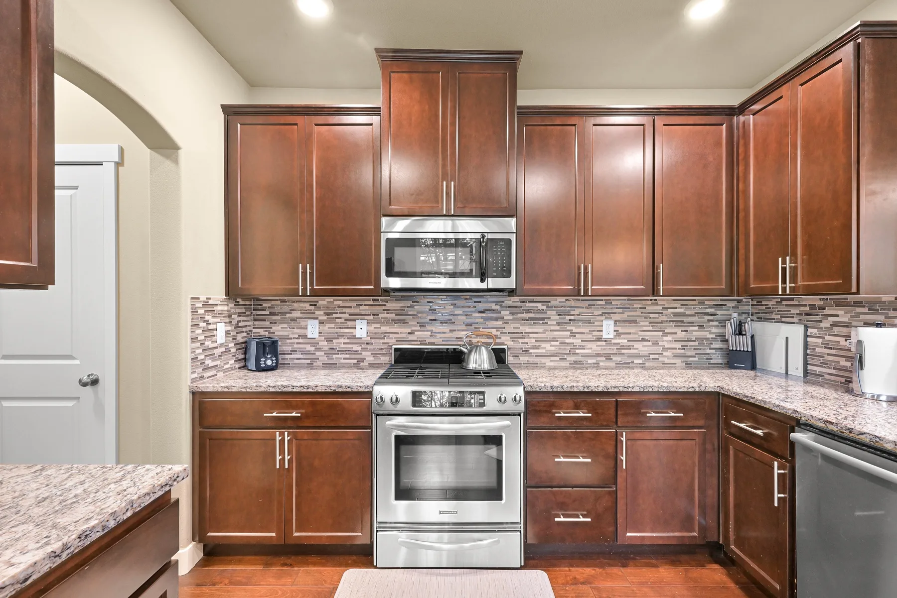 A kitchen with dark wood cabinets, stainless steel appliances, and patterned tile backsplash.