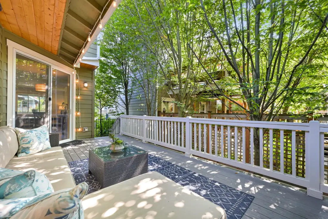 An outdoor deck with seating, a patterned rug, and leafy trees beyond the railing.