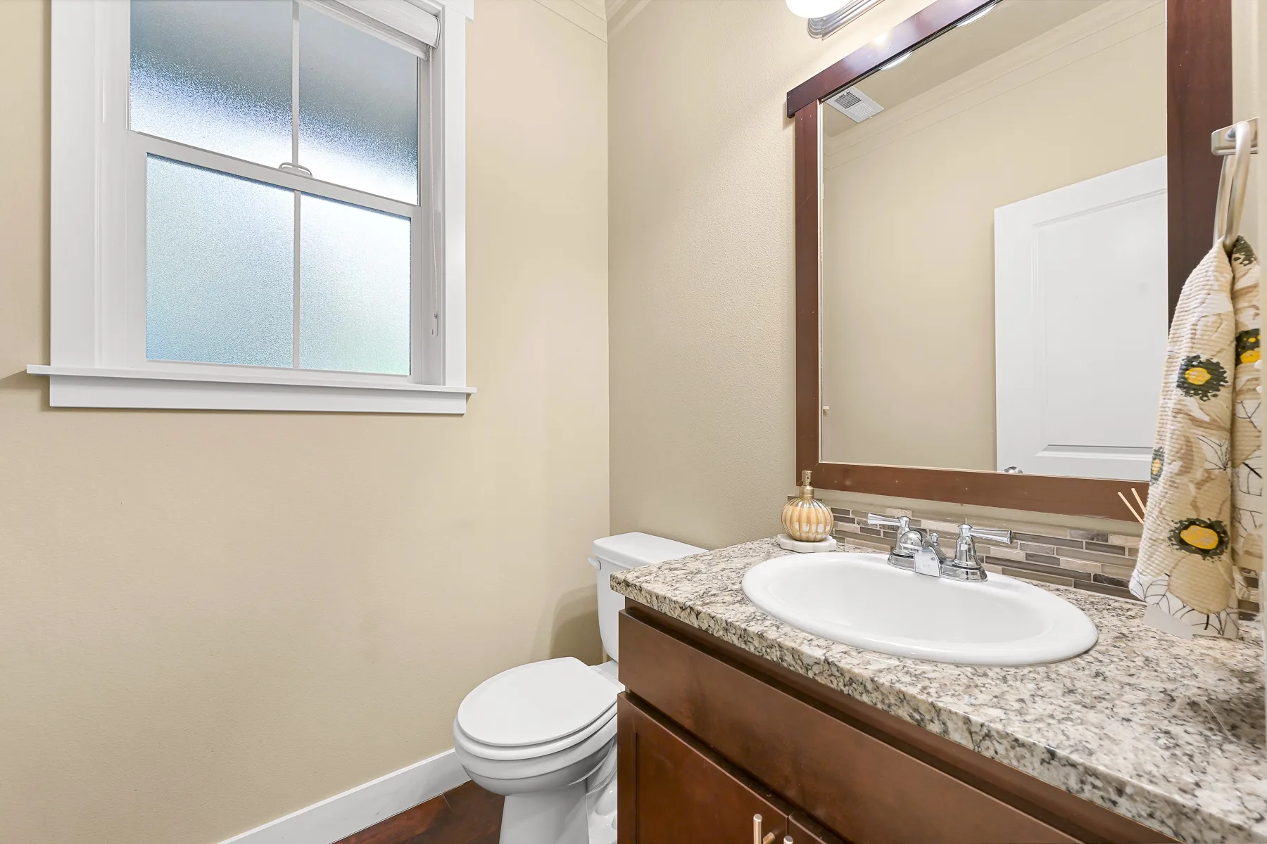 A bathroom vanity with a sink sits beside a toilet and frosted window.