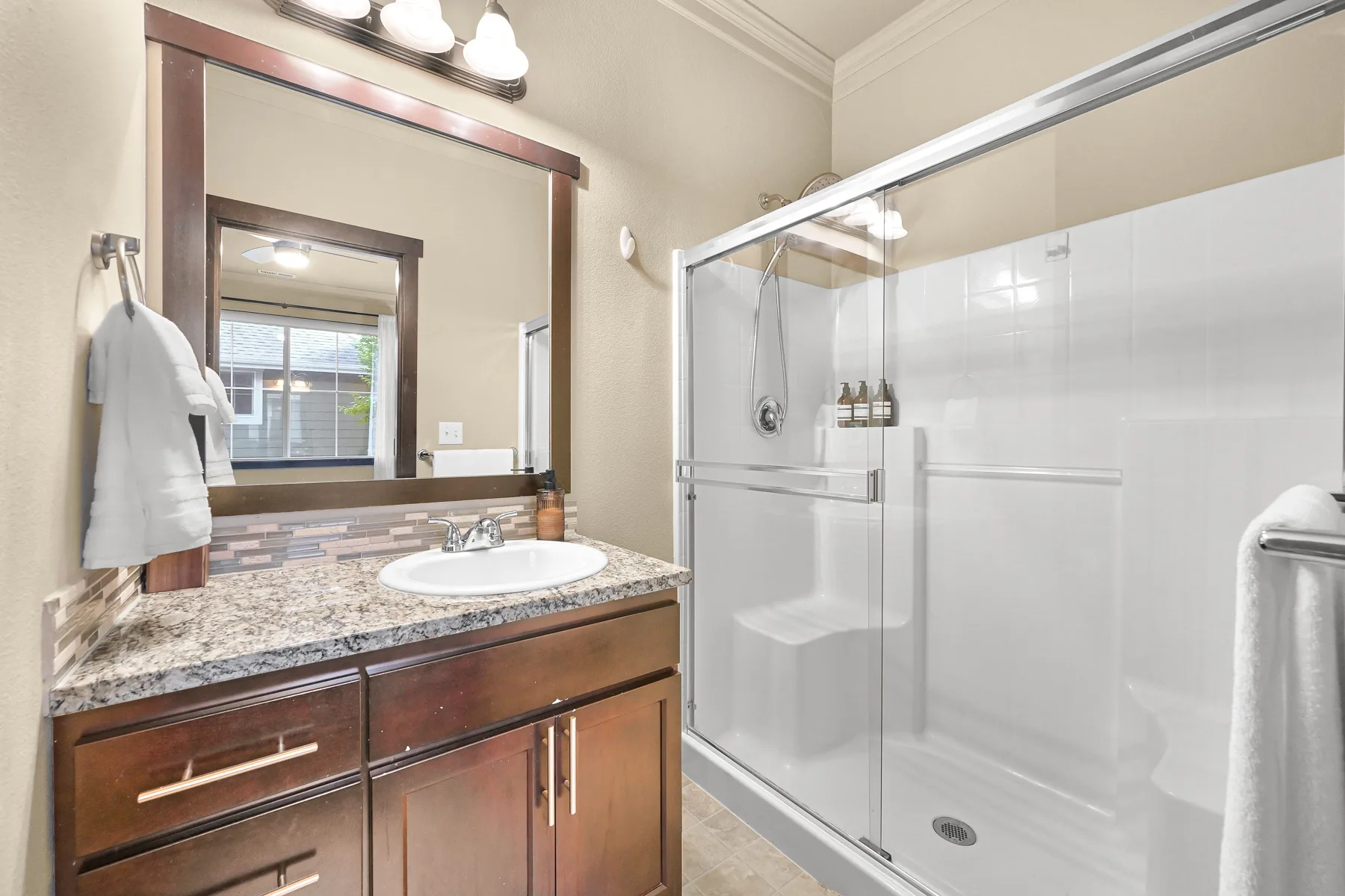 A bathroom vanity with a large mirror stands beside a glass-enclosed shower.