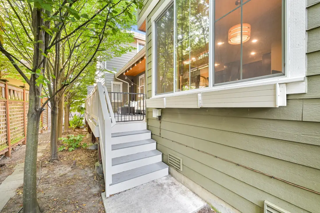 Exterior view of a house with white steps leading to a raised entrance beside large windows.