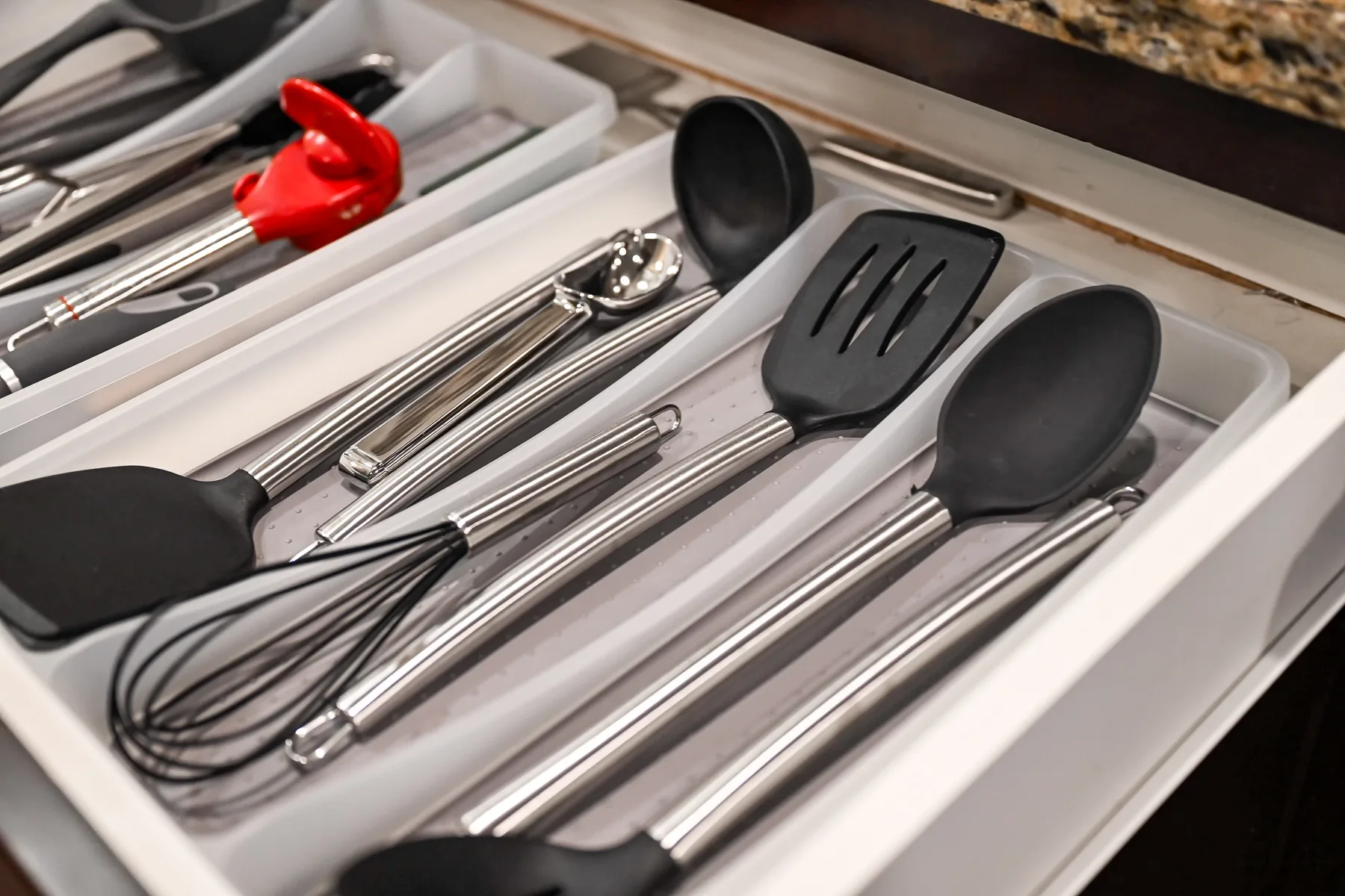 A kitchen drawer holds cooking utensils, including spatulas, a whisk, and serving spoons.