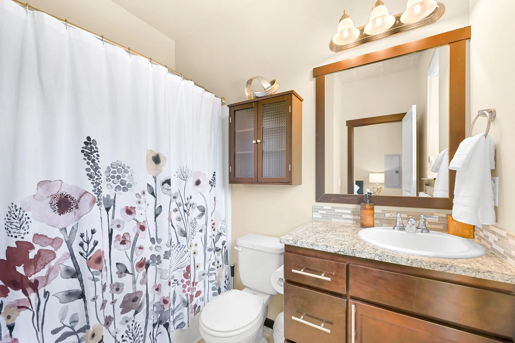 A bathroom vanity with a sink and mirror beside a floral shower curtain.