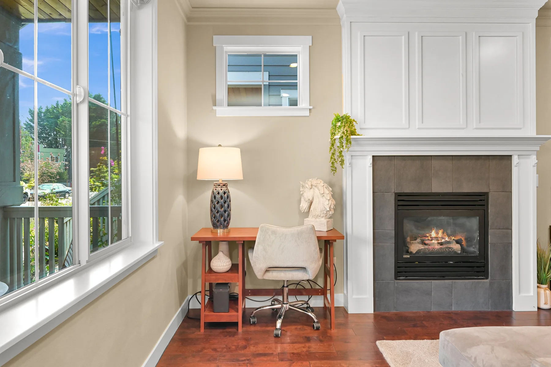 A bright sitting area with a desk beside a fireplace and large windows.